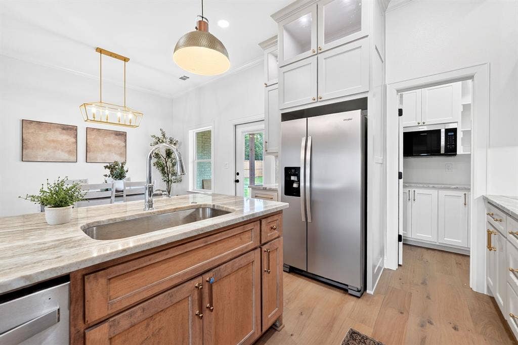 301 Grace Lane, Athens, TX 75751 Gourmet kitchen featuring a large island with an undermount sink, stainless steel appliances, upper cabinetry with glass fronts, light wood-finish flooring, and a walk-in pantry with additional cabinetry