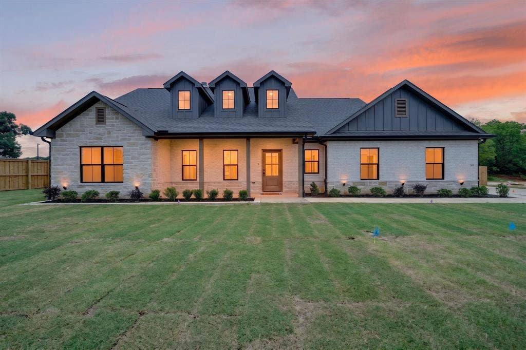 301 Grace Lane, Athens, TX 75751 Modern farmhouse exterior featuring a light-colored stone and siding facade, black-framed windows, dark gray roof, three dormer windows, and a covered porch entry