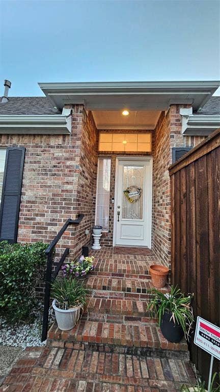 Brick facade entry featuring a covered porch, white paneled door with decorative glass, and brick steps with a black metal handrail