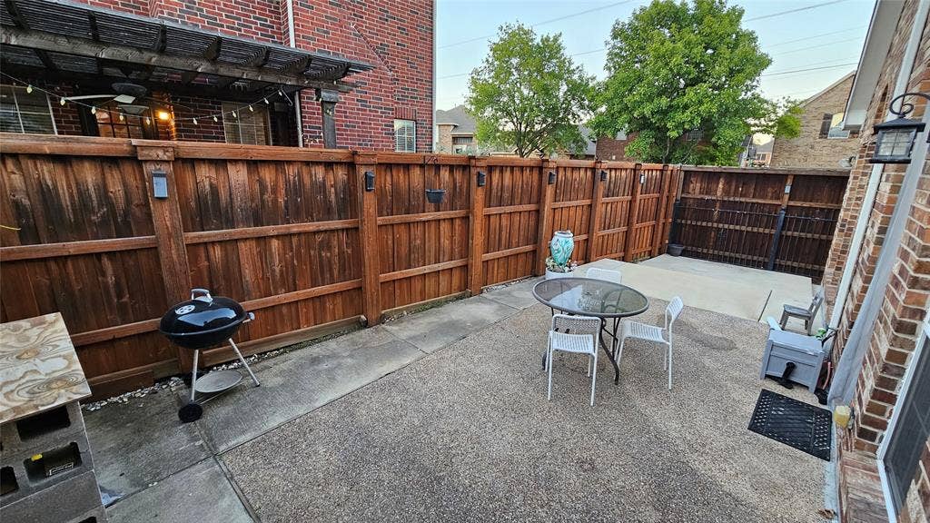 Private outdoor patio area featuring a wooden privacy fence with integrated lighting, exposed aggregate concrete paving, and a brick exterior wall