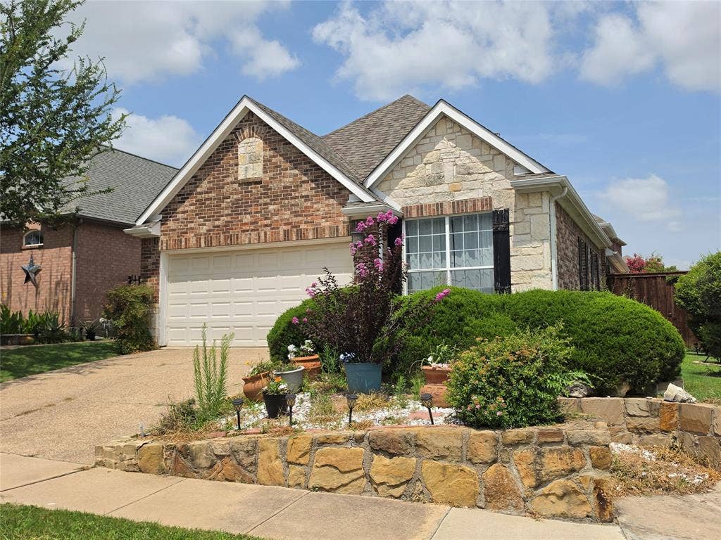 Front exterior featuring a brick and stone facade, an attached garage, and a tiered stone retaining wall