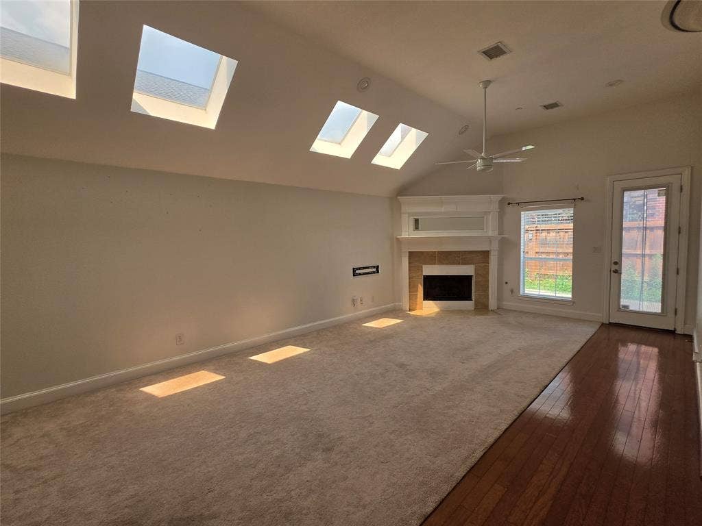 Spacious interior featuring a vaulted ceiling with multiple skylights, a fireplace with a mantel, a ceiling fan, and mixed flooring with carpet and wood-finish