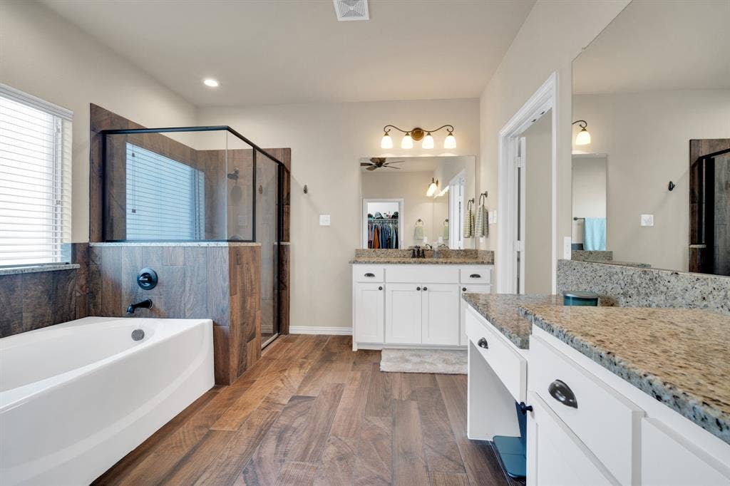 Primary en suite bathroom. Separate vanities with granite countertops. Wood grain look ceramic tile floors  and shower walls. Garden soaker tub.
