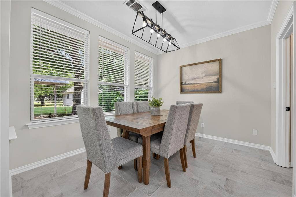 Bright interior room featuring a modern linear chandelier, crown molding, and light gray wall paint