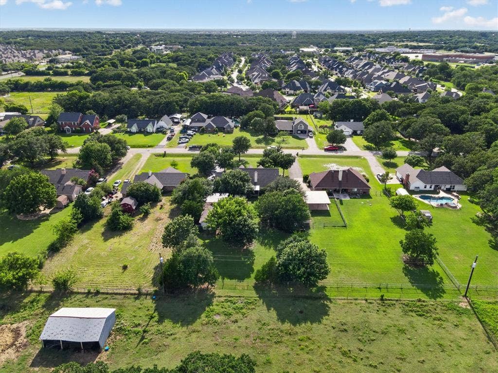 Expansive lot featuring a large green space, mature trees, and a distant neighborhood