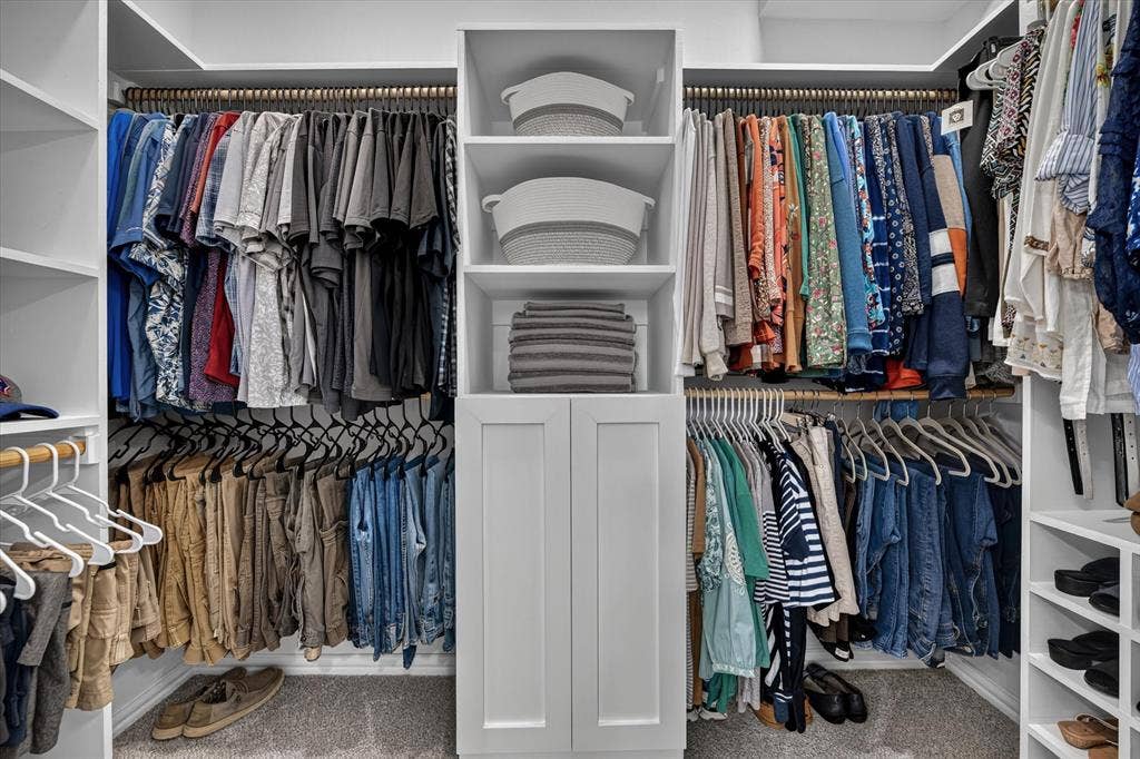 Custom closet system featuring white built-in cabinetry, open shelving, and multiple hanging rods
