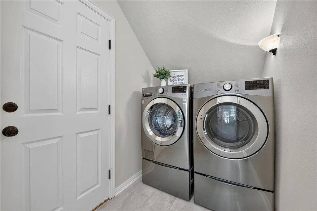 Dedicated laundry area featuring light gray walls, a white paneled door with dark hardware, and light-toned tile flooring