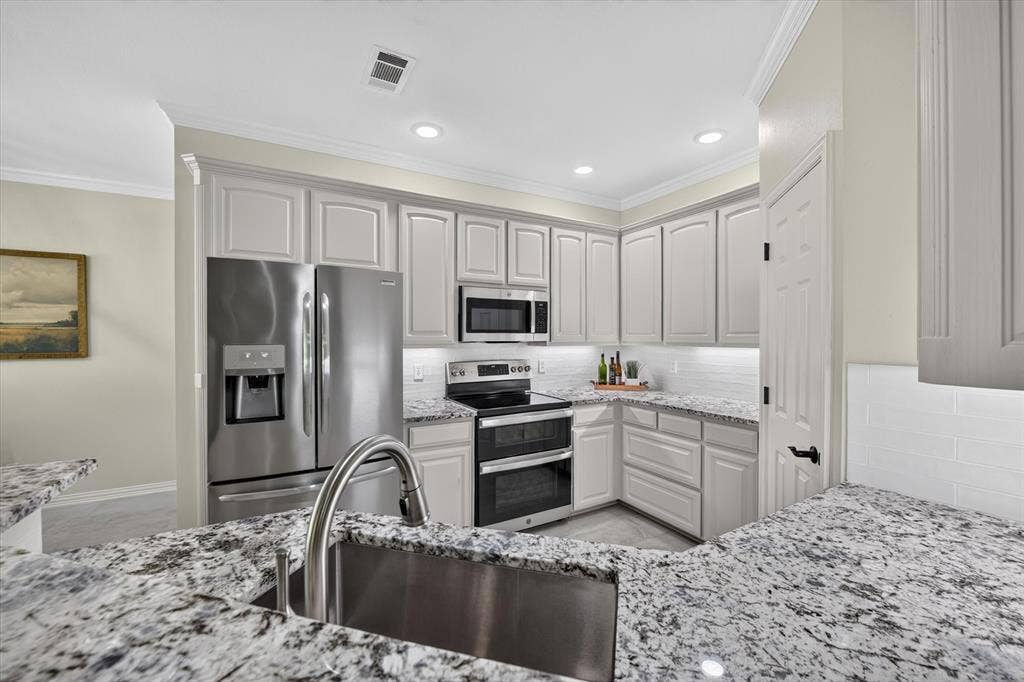 Kitchen featuring granite countertops, stainless steel appliances, white shaker cabinetry, white subway tile backsplash, and a large undermount sink with a gooseneck faucet