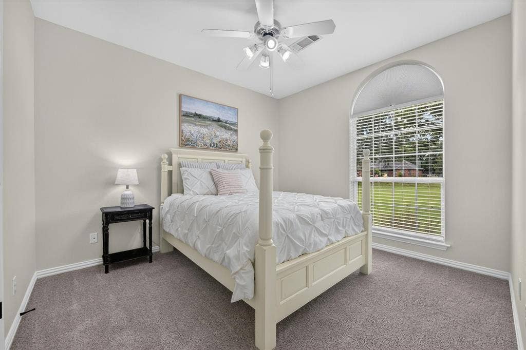 Carpeted room featuring a large arched window, a ceiling fan with integrated lighting, neutral wall paint, and white baseboards