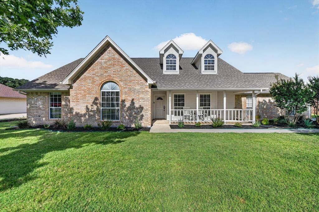 Exterior featuring brick and siding finishes, a covered front porch with white railing, dormer windows, and a manicured lawn