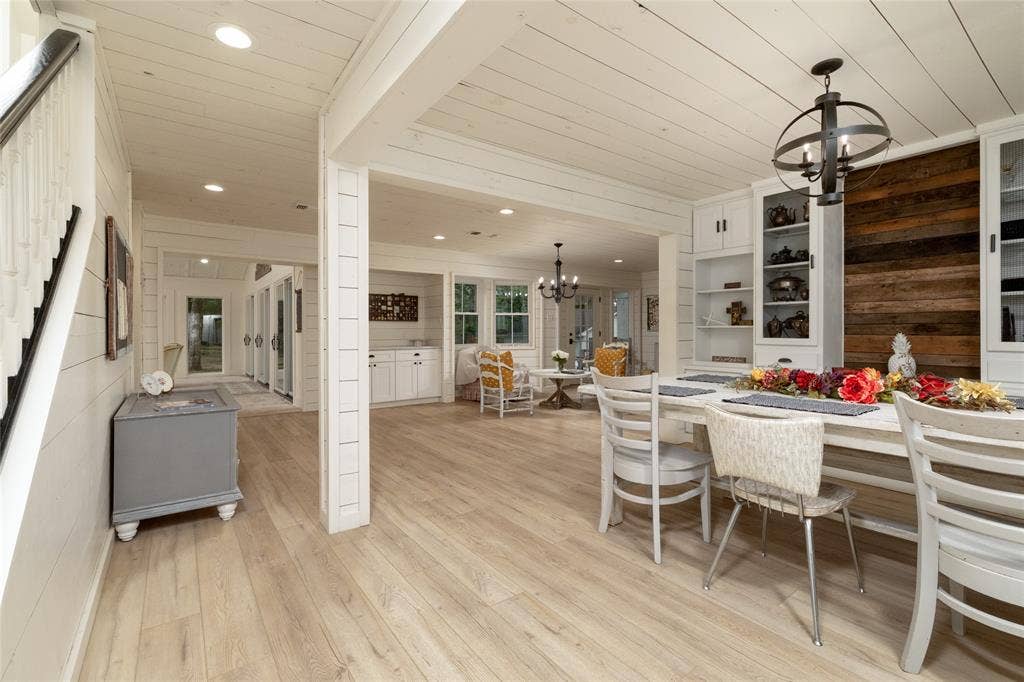 Spacious interior featuring light wood-finish flooring, white shiplap walls and ceiling, recessed lighting, and a white staircase with a dark wood handrail
