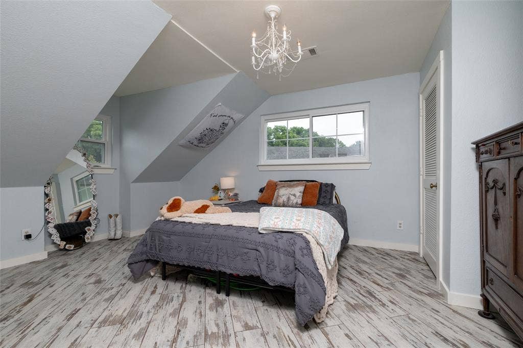 Attic bedroom featuring pitched ceilings, wood-finish flooring, multiple windows, a louvered bi-fold door, and a decorative chandelier