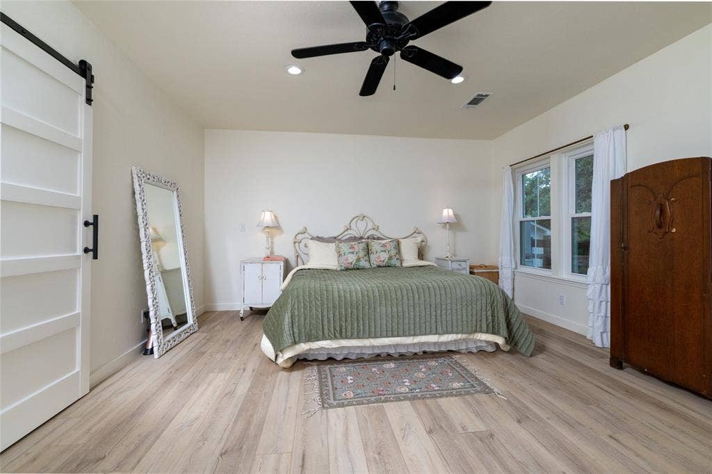 Bright room with wood-finish flooring, a white barn door, recessed lighting, and a ceiling fan