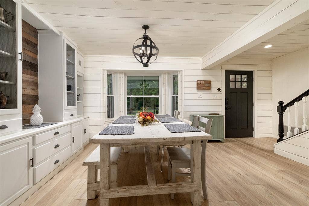 Spacious dining area featuring white shiplap walls, wood-finish flooring, and a large bay window
