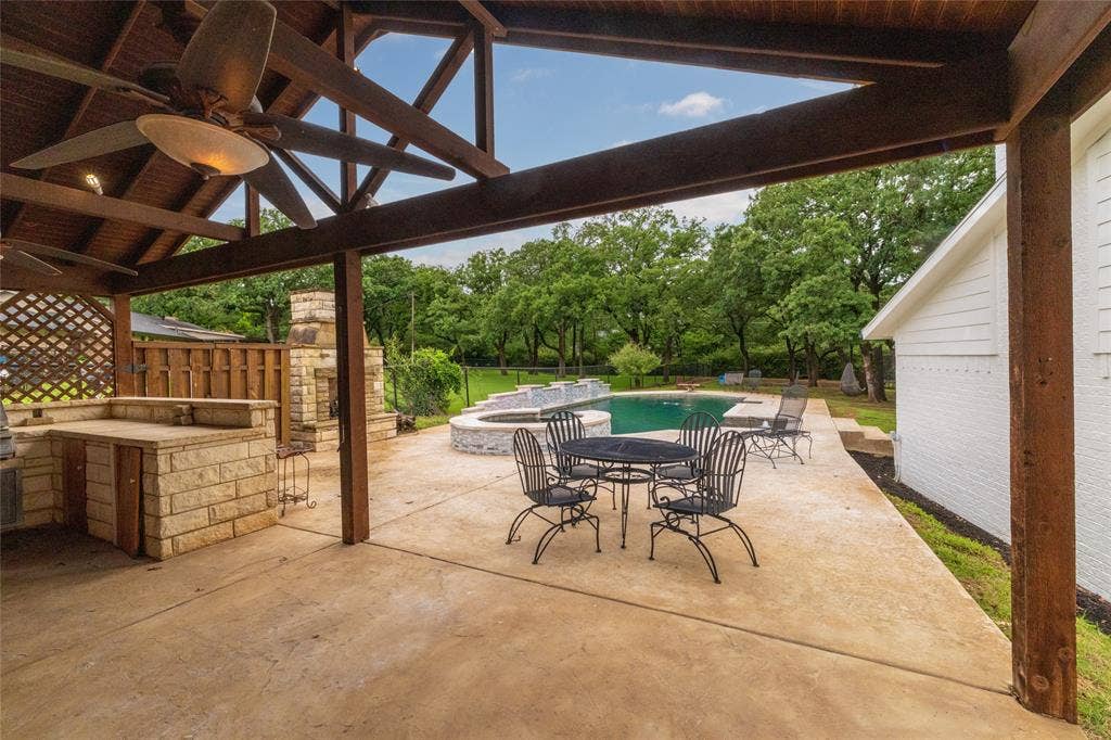 Covered patio featuring an outdoor kitchen with stone base, a stone fireplace, and exposed wood beam ceiling with ceiling fans