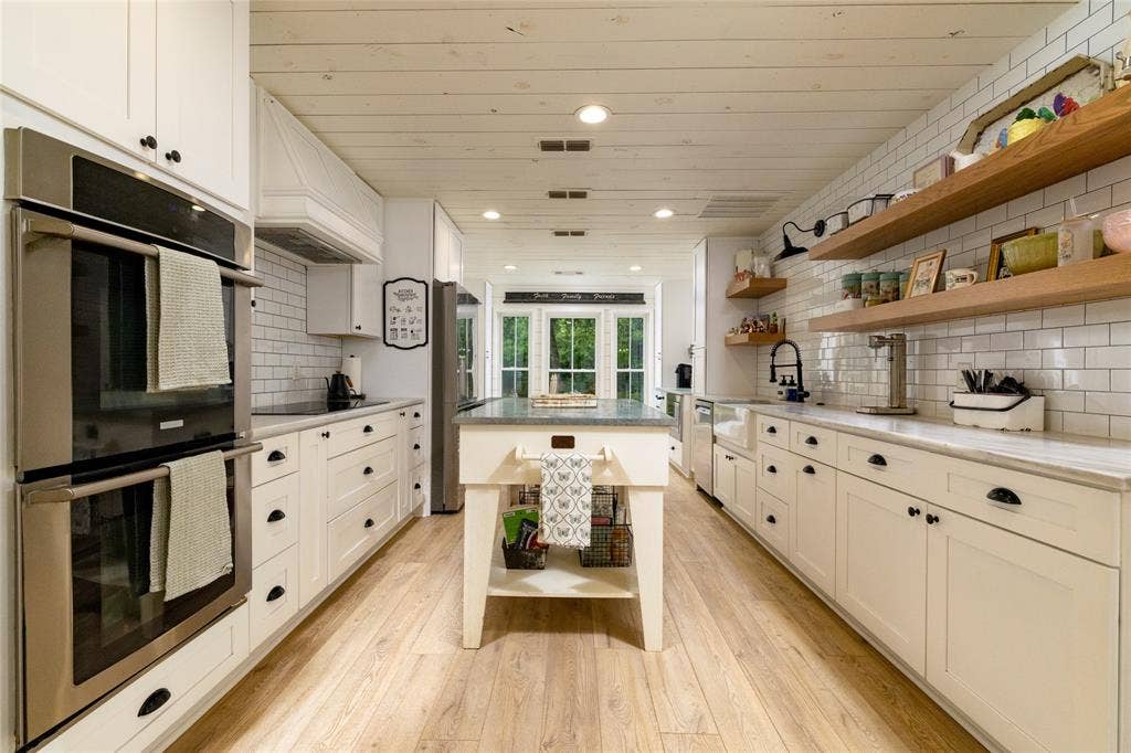 Sleek kitchen featuring wood-finish flooring, white subway tile backsplash, and extensive white cabinetry with black hardware