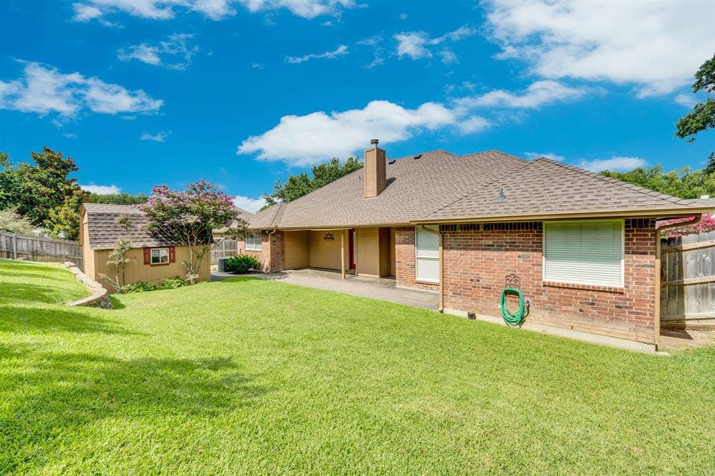 Expansive backyard featuring a lush lawn, a detached storage building with a shingled roof, a covered patio, and a brick exterior