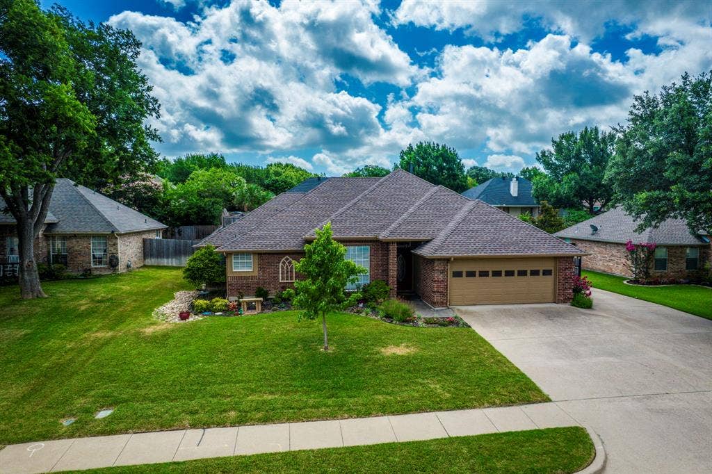 Brick exterior residence with a two-car garage, concrete driveway, and mature landscaping