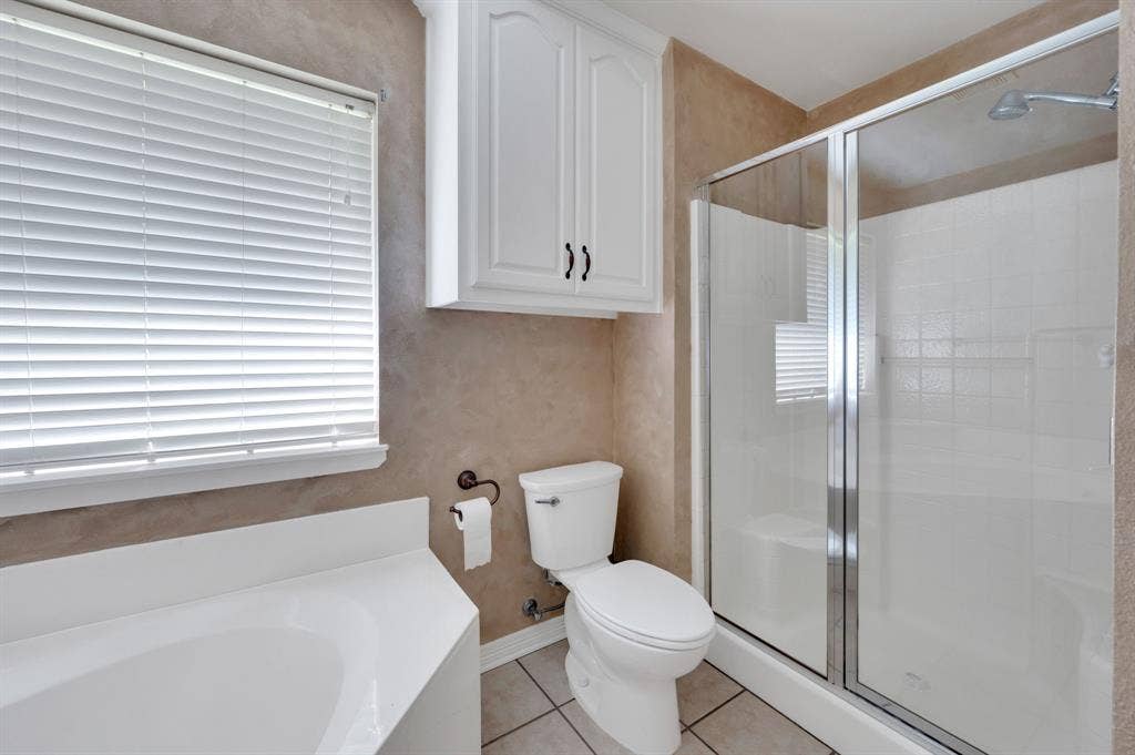 Bathroom featuring a built-in tub, tiled shower with glass enclosure, white cabinetry, and a window with blinds