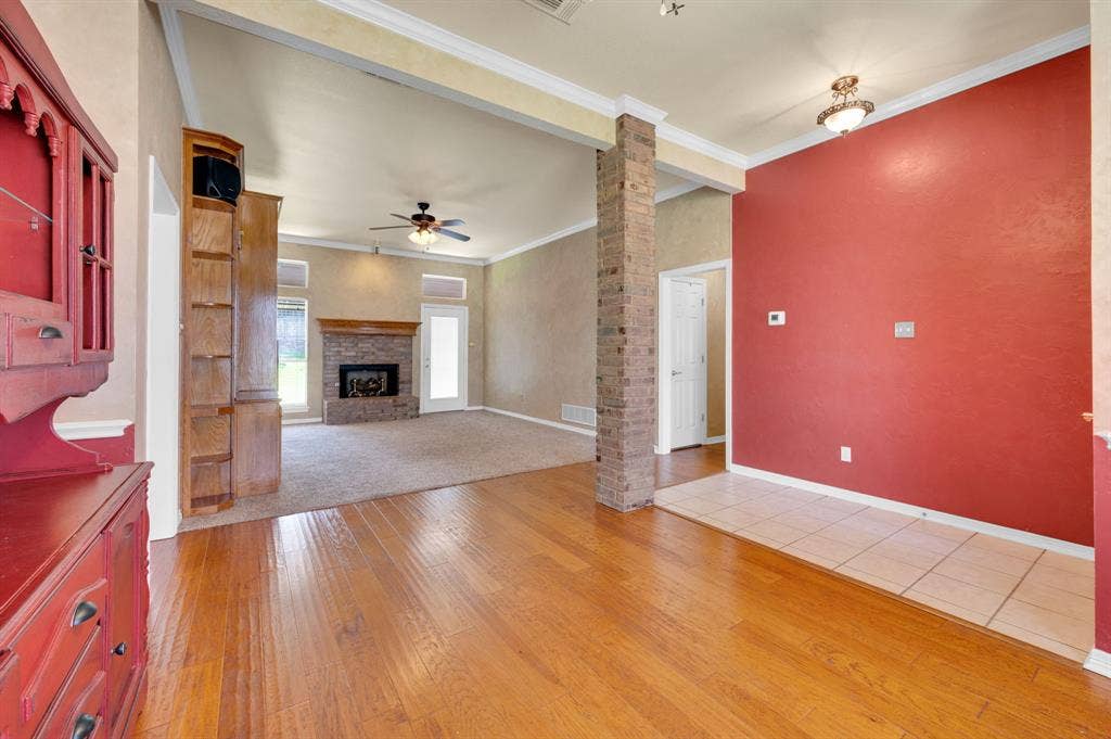 Wood-finish flooring leading to a carpeted living area with a stone-clad fireplace and wood mantel