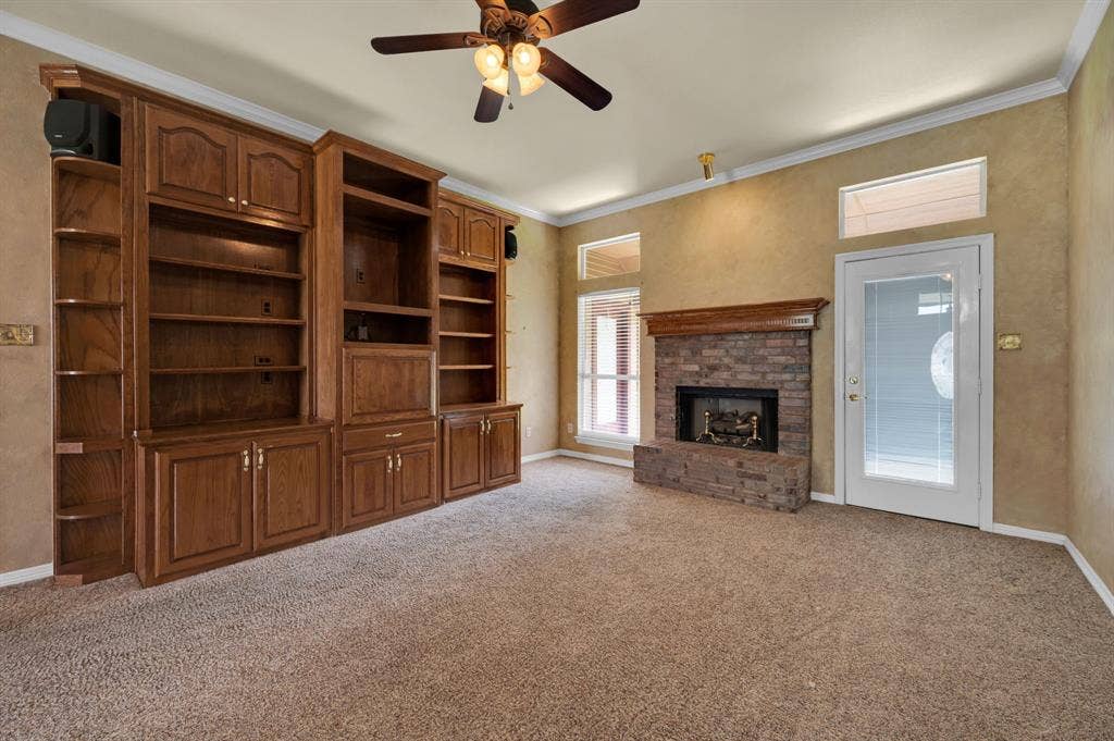 Spacious living area featuring extensive built-in cabinetry, a stone-faced fireplace with a wood mantle, and a ceiling fan