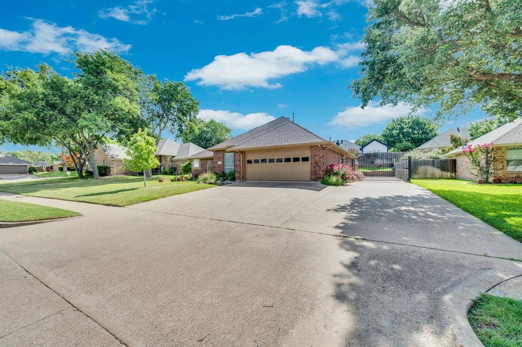Brick exterior home with an attached garage, featuring a concrete driveway and mature trees