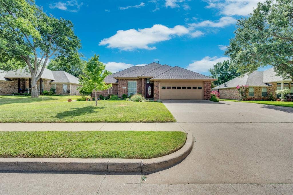 Brick facade home featuring a two-car garage, mature front yard landscaping, an asphalt driveway, and a shingle roof