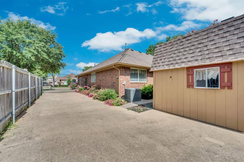 Paved driveway leading to a detached structure with a shingle roof and decorative red shutters