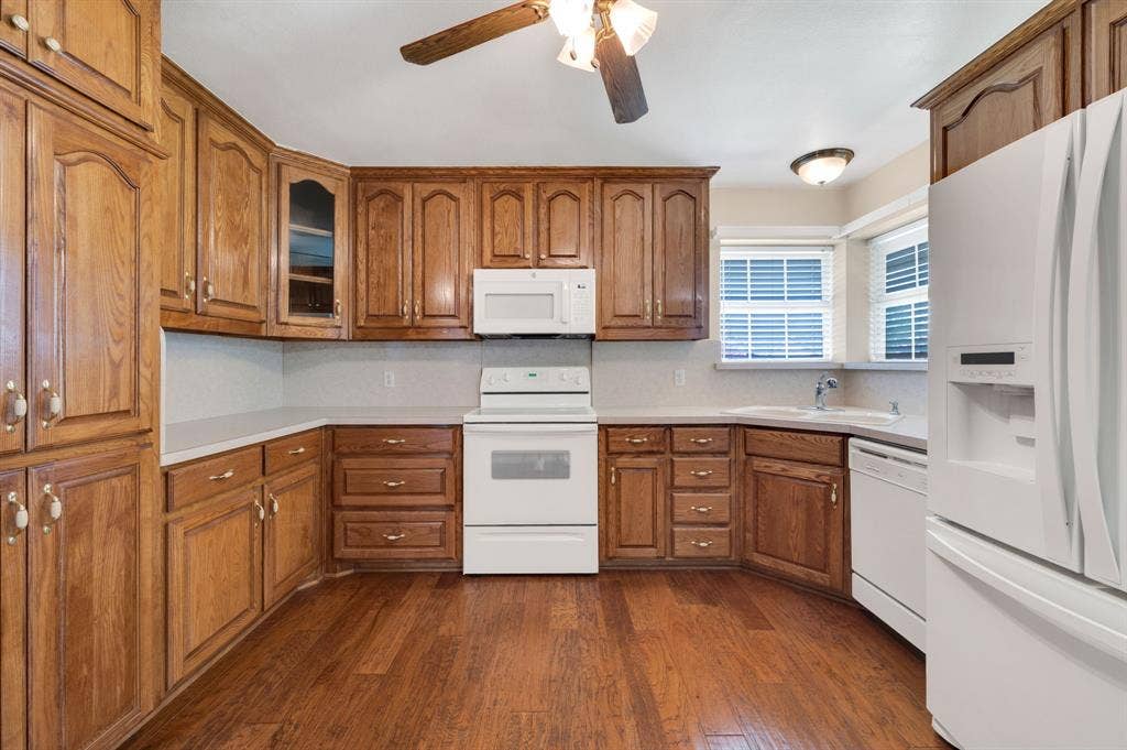 Kitchen featuring wood-finish flooring, extensive wood cabinetry, white appliances, light countertops, and a window with blinds