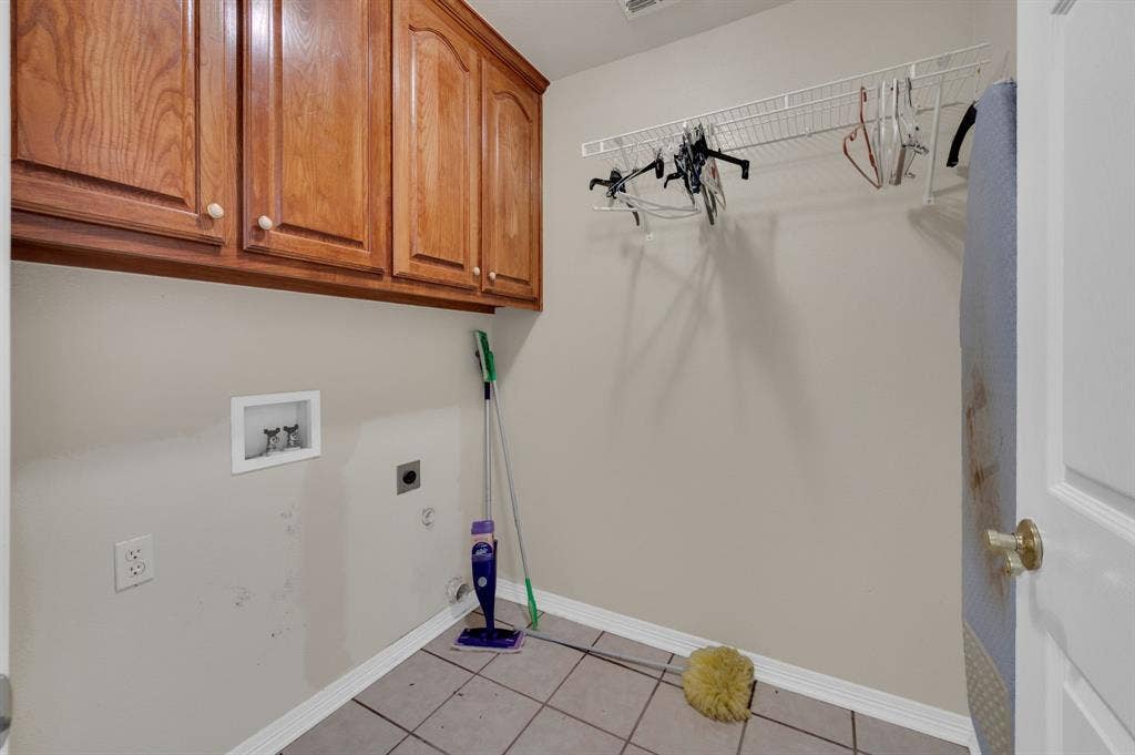 Utility room featuring wood-finish cabinetry, tile flooring, and a wall-mounted wire shelving system