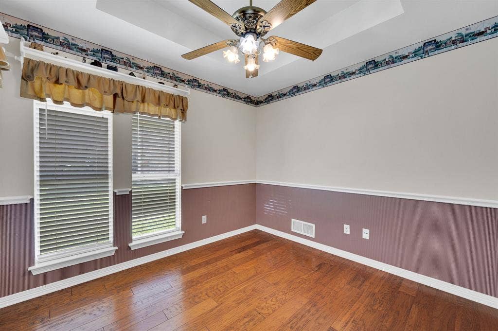 Dining area or Office space  featuring wood-finish flooring, two large windows with blinds, a ceiling fan with integrated lighting, and a tray ceiling