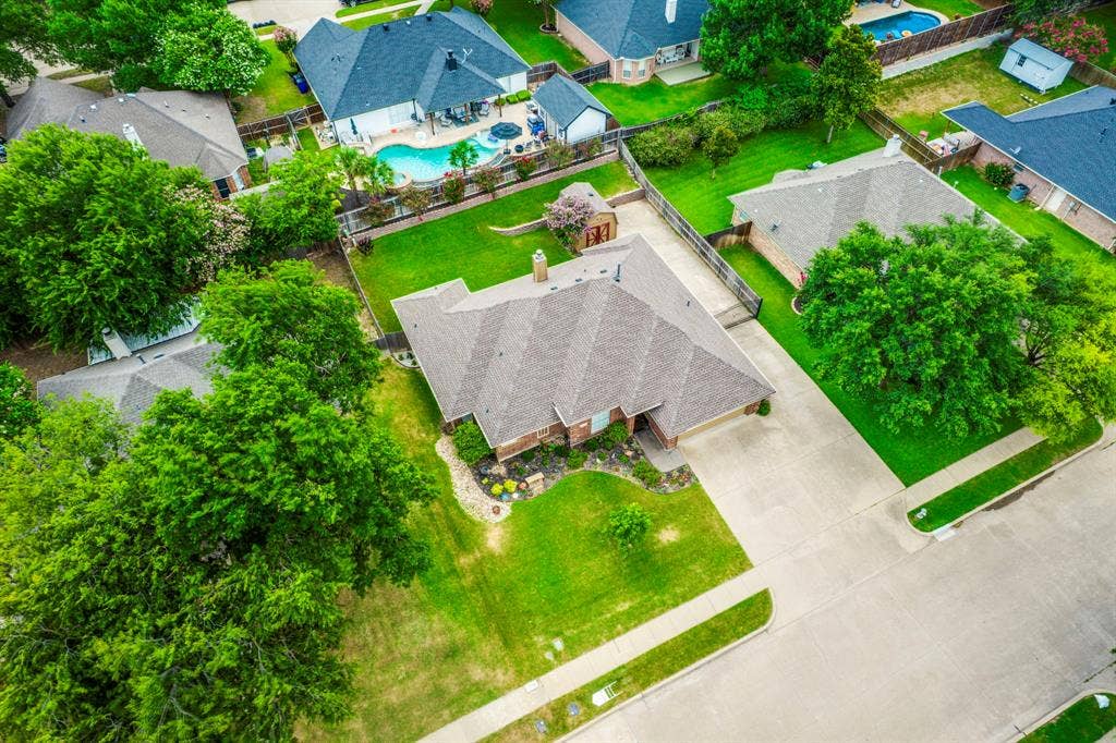 Aerial view highlighting the property with a brown shingle roof, brick exterior, and an attached two-car garage