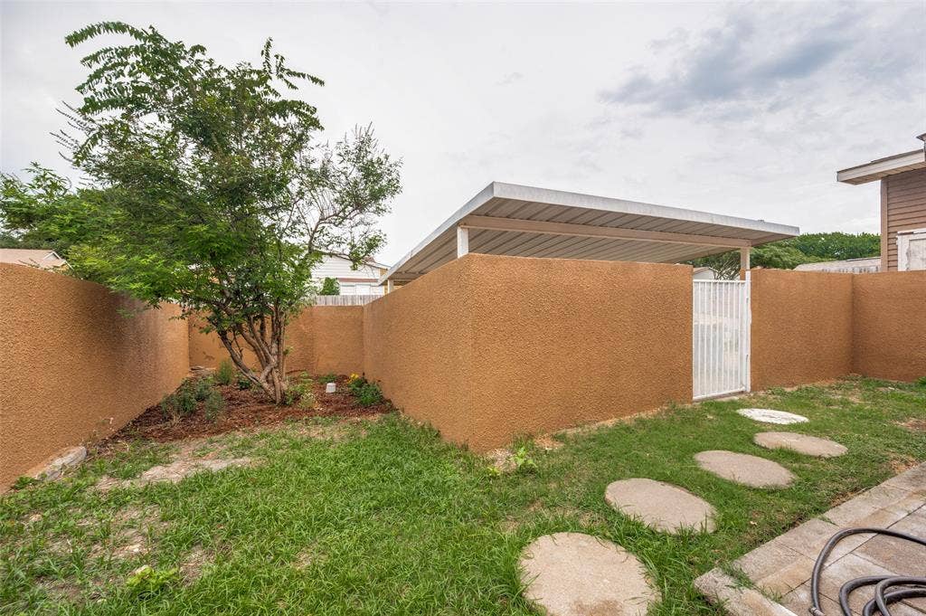 412 Pogue Street, Cedar Hill, TX 75104 Private backyard featuring textured stucco walls, a mature tree, round stepping stones, and a covered patio structure