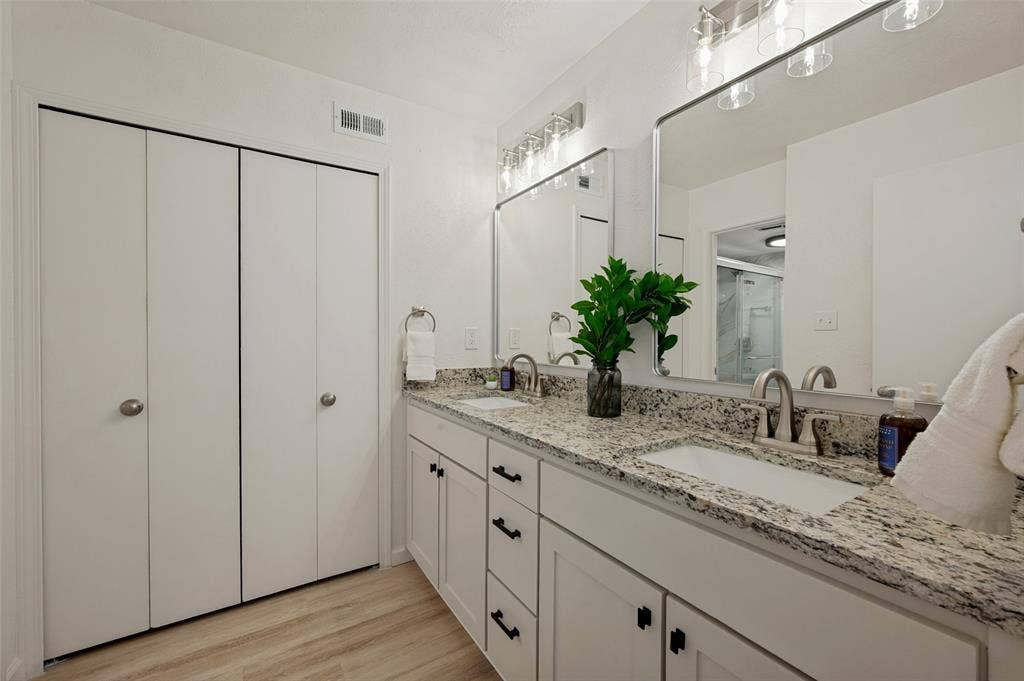 412 Pogue Street, Cedar Hill, TX 75104 Bathroom featuring a double vanity with granite-finish countertops, white cabinetry with black hardware, dual undermount sinks, and wood-finish flooring