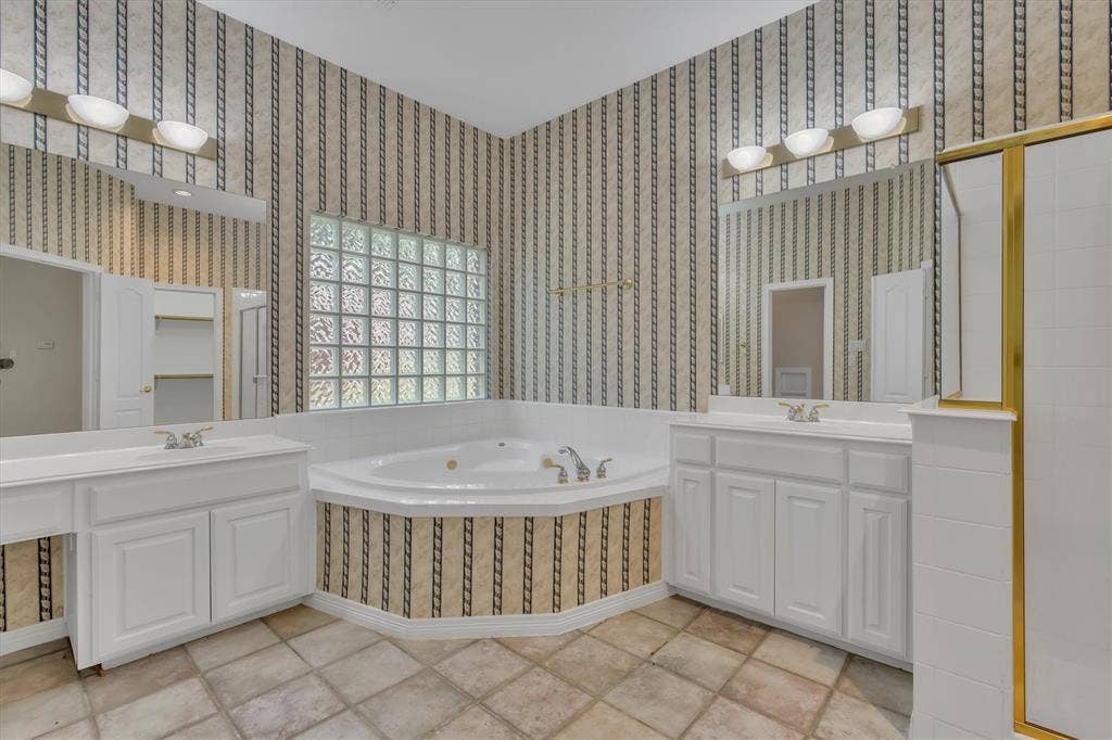 Primary Bathroom featuring a corner soaking tub, a glass block window, and dual vanities with integrated sinks