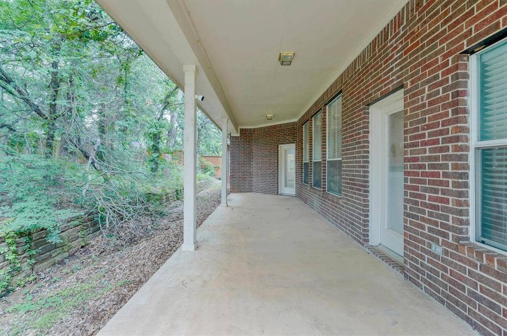Back  Covered patio with a concrete surface and multiple access points, featuring a brick exterior and a stone retaining wall