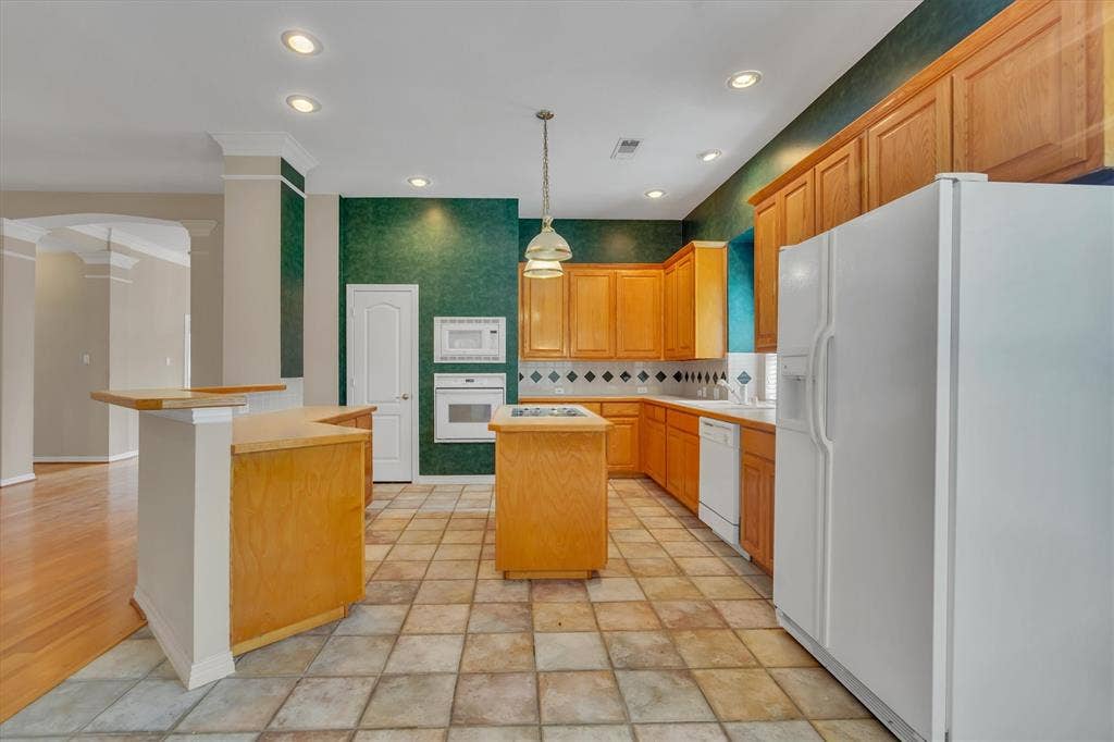 Kitchen featuring tile flooring, light wood cabinetry, a central island, recessed lighting, and built-in white appliances