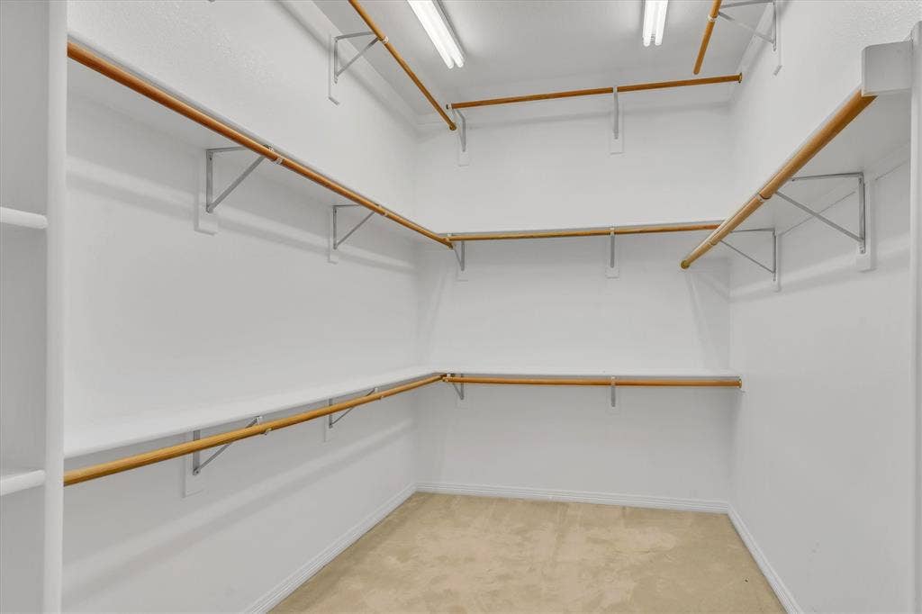 Primary Bedroom Walk-in closet featuring built-in shelving, multiple hanging rods, white walls, and light-colored carpet flooring