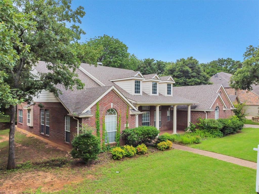 Brick exterior featuring an arched window, a gabled roofline, a concrete driveway, a wooden privacy fence, and a stone retaining wall
