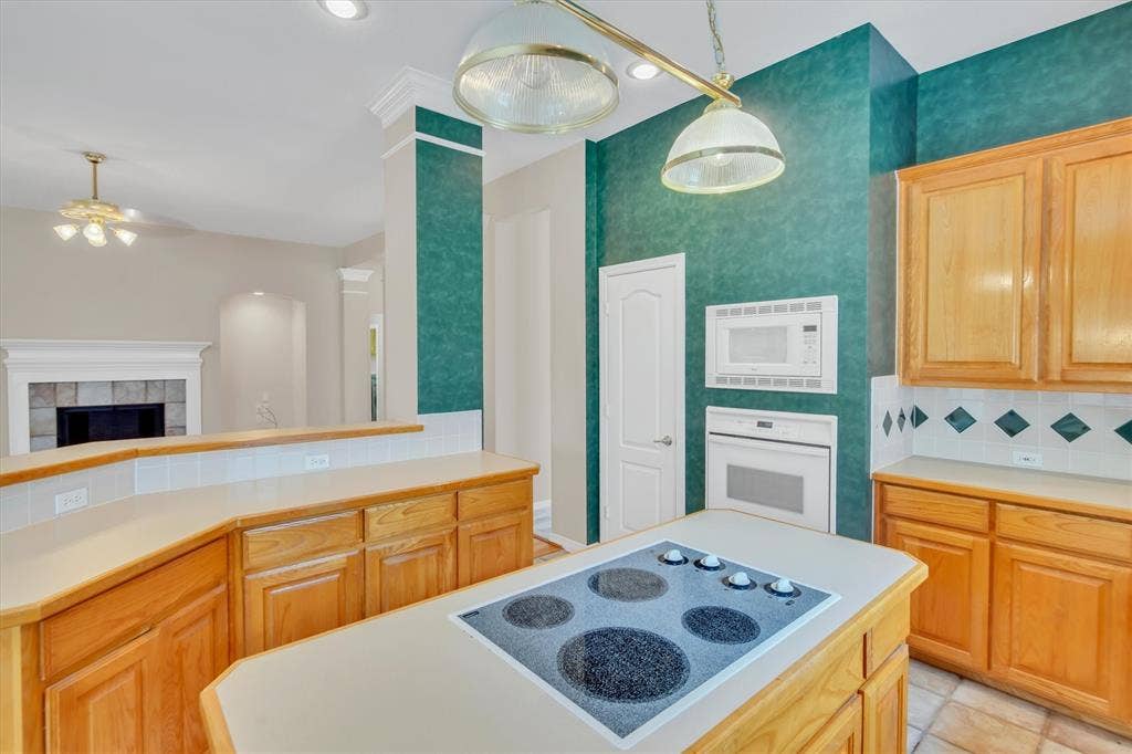 Kitchen featuring a built-in cooktop island, light wood cabinetry, white tile backsplash with diamond accents, wall-mounted microwave, and a built-in oven