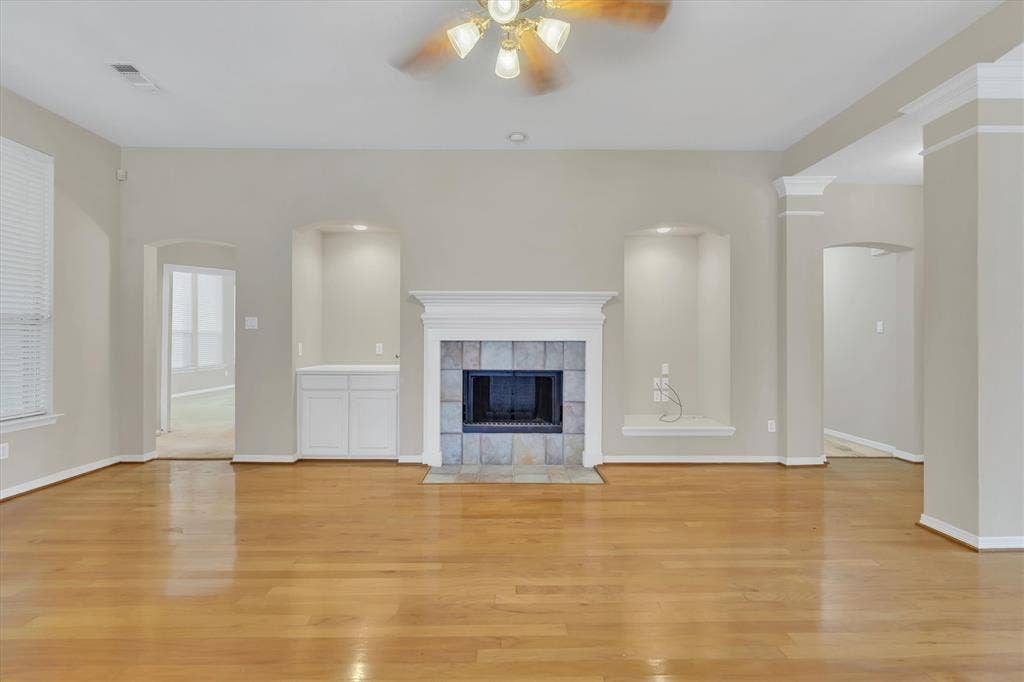 Living area with wood-finish flooring, a fireplace featuring a tile surround and white mantel, built-in cabinetry, and recessed wall niches