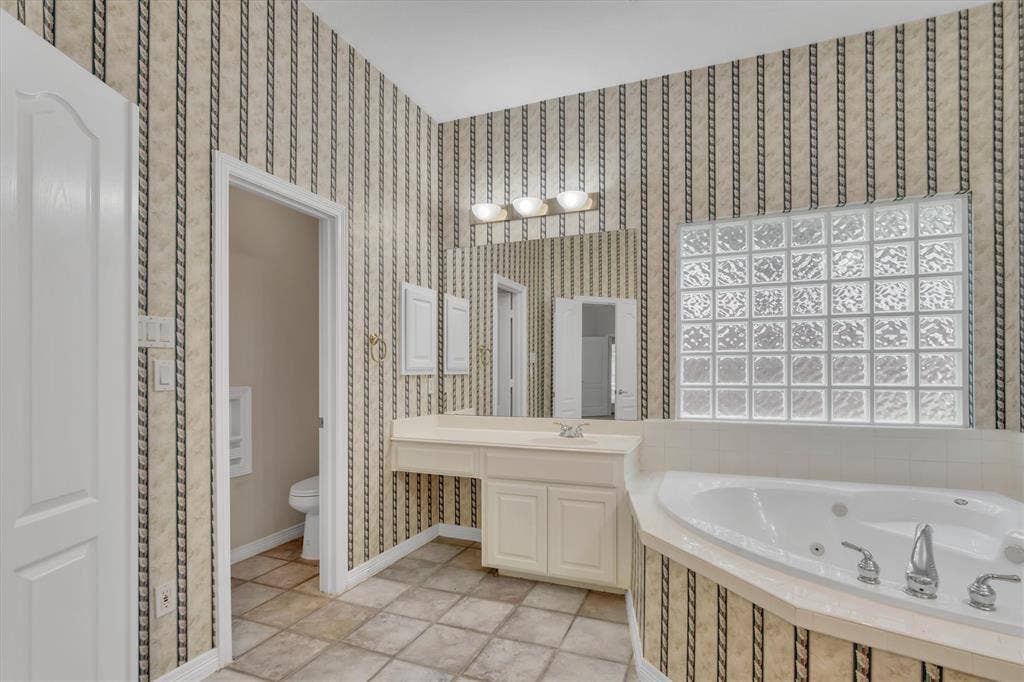 Primary Bathroom featuring a built-in jetted tub, glass block window, vanity with integrated sink, and an extensive mirror