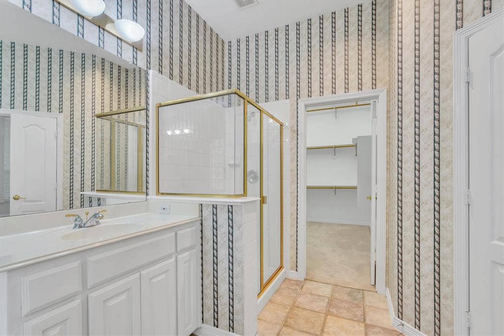Primary Bathroom featuring a single vanity with integrated sink, gold-framed shower enclosure, patterned wallpaper, and a separate closet with shelving