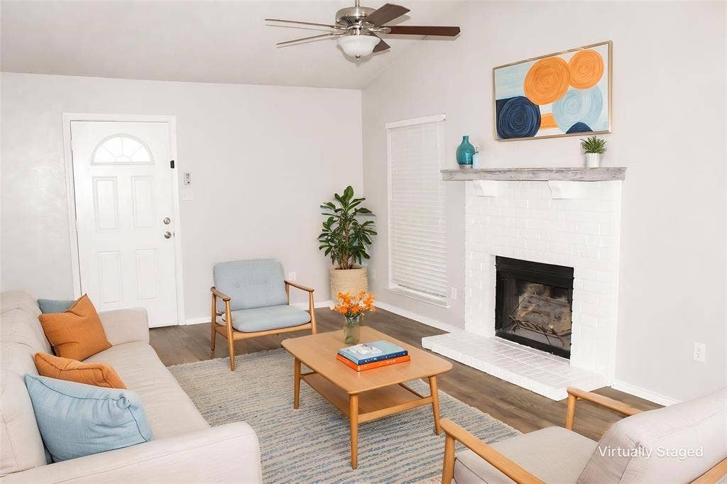 Vaulted ceiling with a ceiling fan, wood-finish flooring, white brick fireplace with a mantel, and a paneled entry door with an arched window