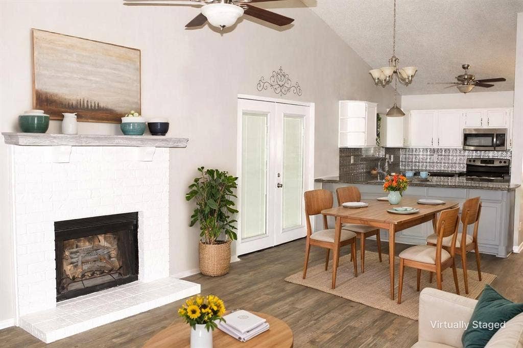 Virtually staged, vaulted ceiling, wood-finish flooring, white brick fireplace, glass-panel French doors, and a kitchen with white cabinetry and a backsplash