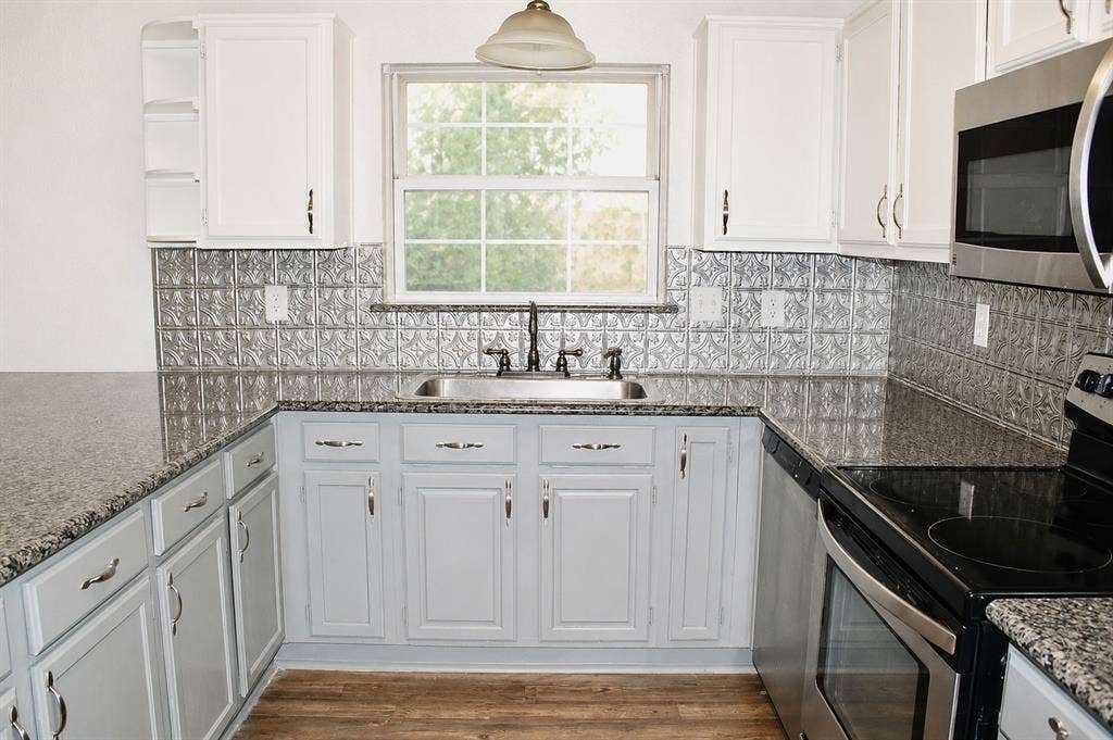 U-shaped kitchen featuring granite-look countertops, stainless steel appliances, a tin-look backsplash, and wood-finish flooring
