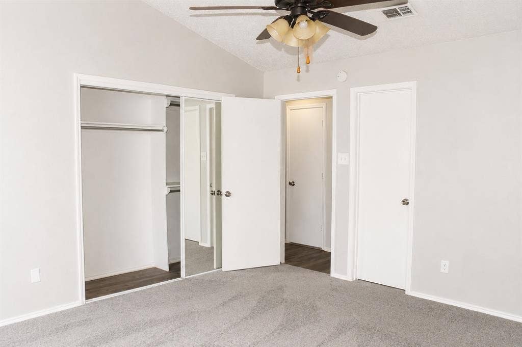 Vaulted ceiling with a ceiling fan, light gray wall paint, gray carpet flooring, sliding mirrored closet doors, and wood-finish flooring in the doorway