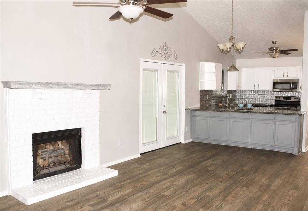 Wood-finish flooring throughout, vaulted ceiling, white brick fireplace, French doors, and a kitchen with white upper and grey lower cabinetry