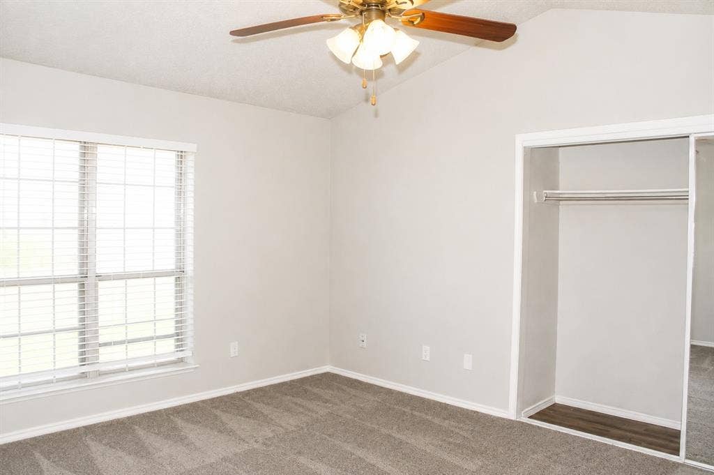 Vaulted ceiling, ceiling fan with integrated lighting, window with horizontal blinds, built-in closet with sliding mirrored doors, and carpet flooring