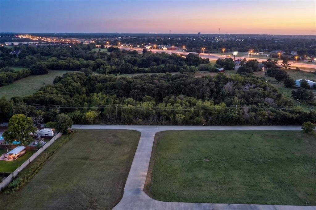 Expansive cleared lot with a paved entry, bordered by natural tree lines